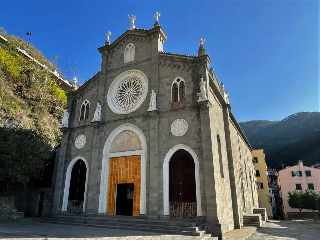 Church of Saint John the Baptist in Riomaggiore, Italy.  Gray brick church with white saint statues on building